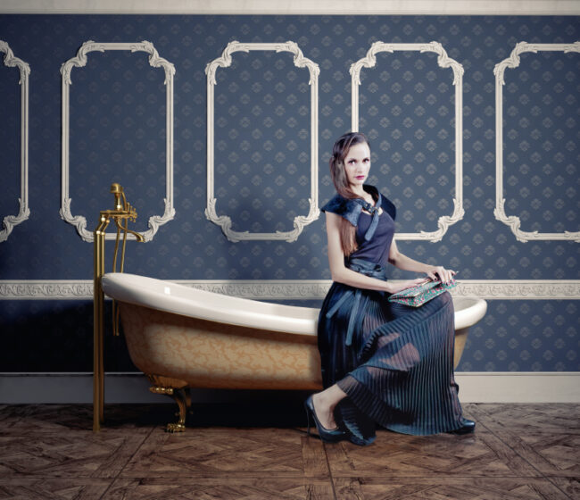 Frau in Kleid auf Badewanne vor klassischer blauer Tapete